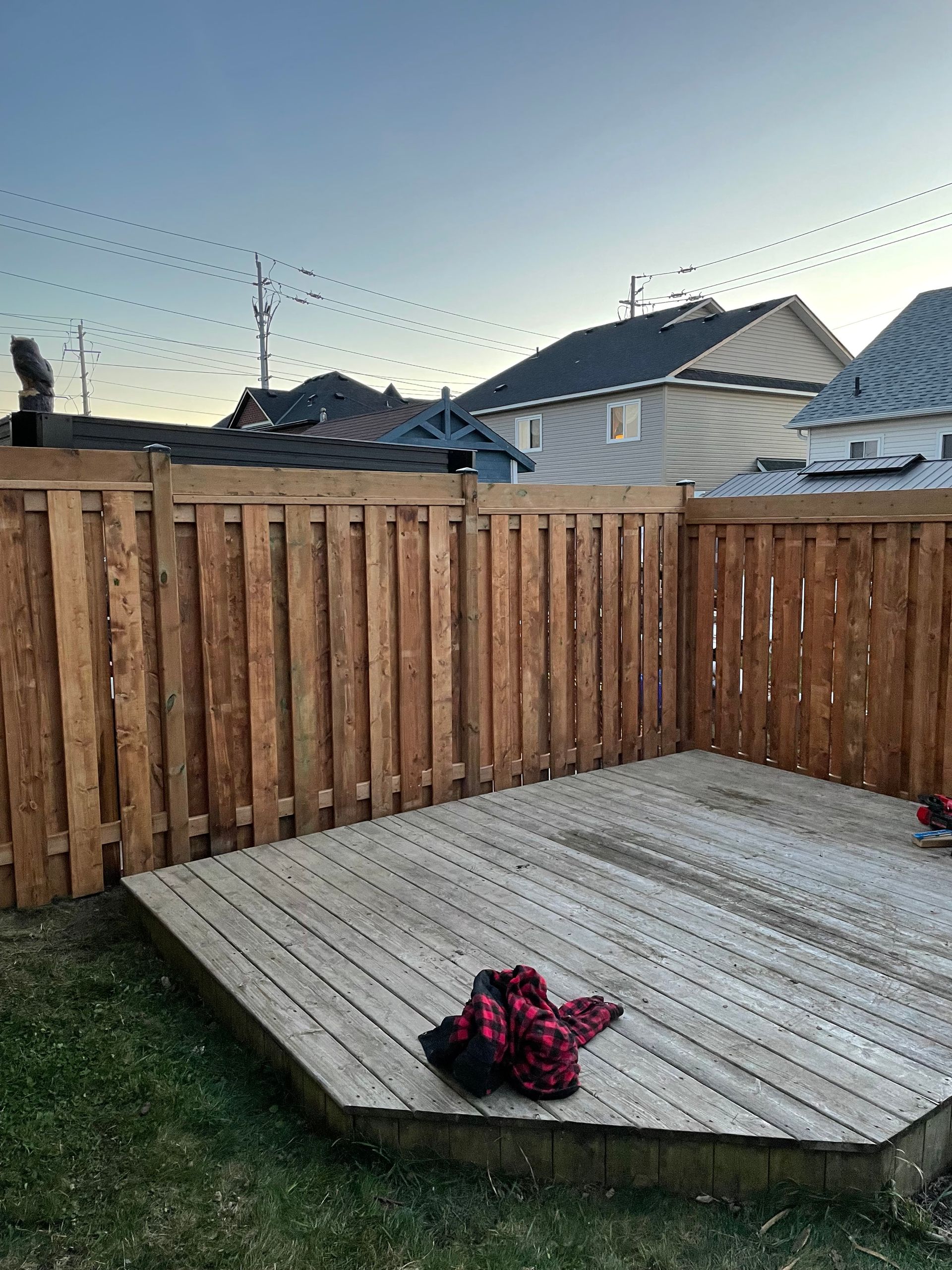 A wooden fence surrounds a wooden deck in a backyard.