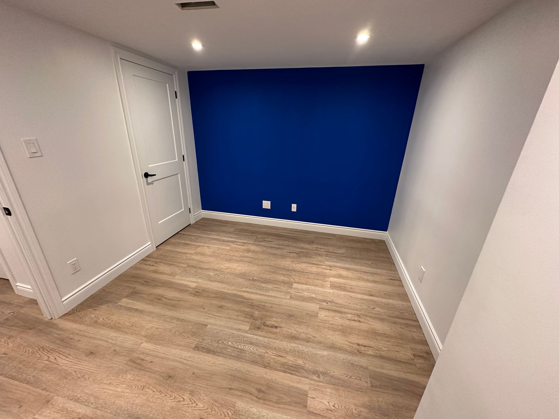 An empty room with a blue wall and wooden floor.