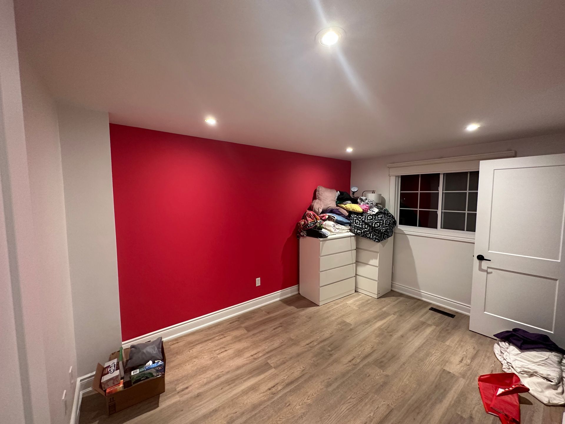 A room with a red wall and a pile of clothes on the floor.