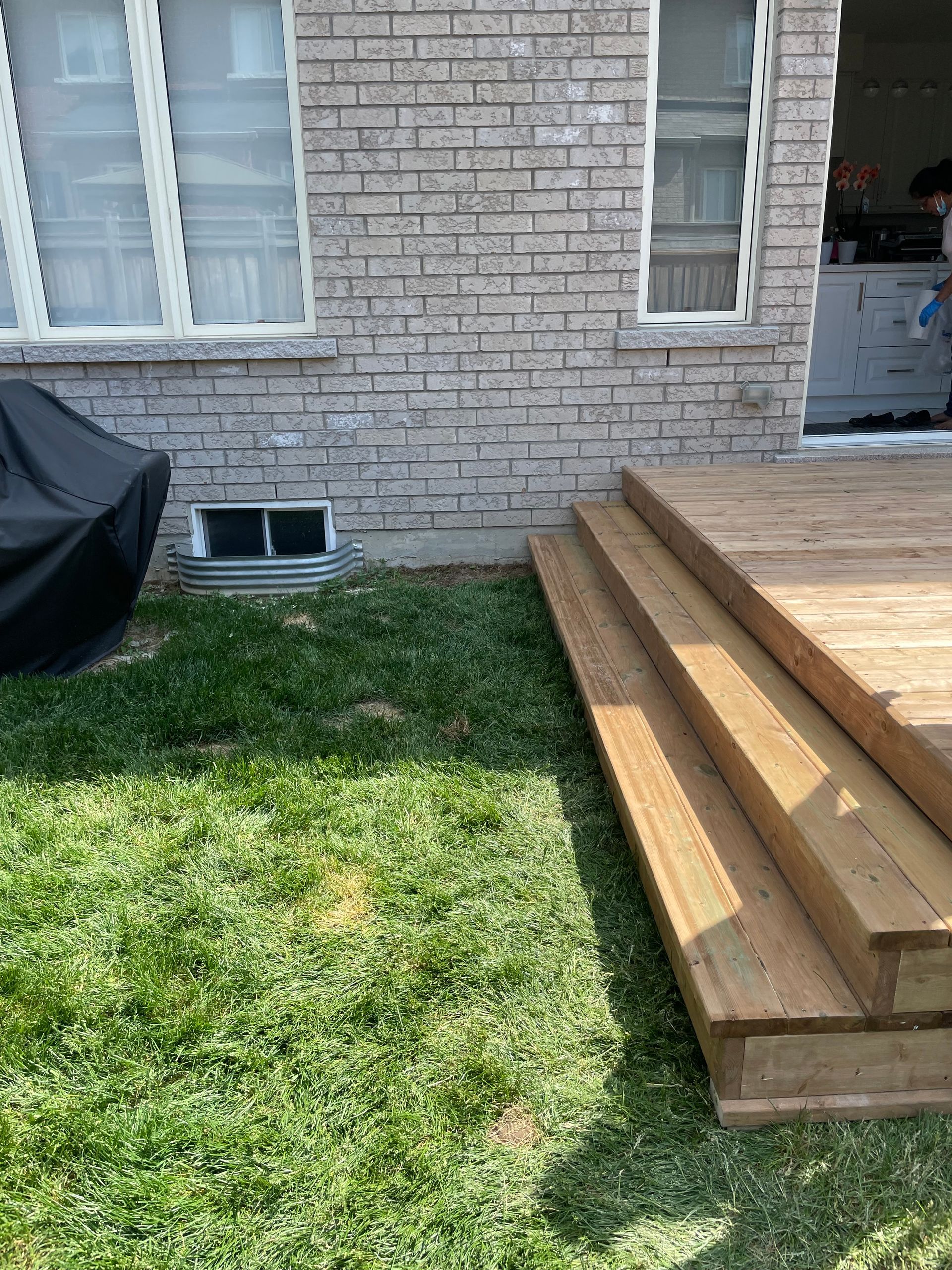 A wooden deck is sitting in the grass in front of a brick house.
