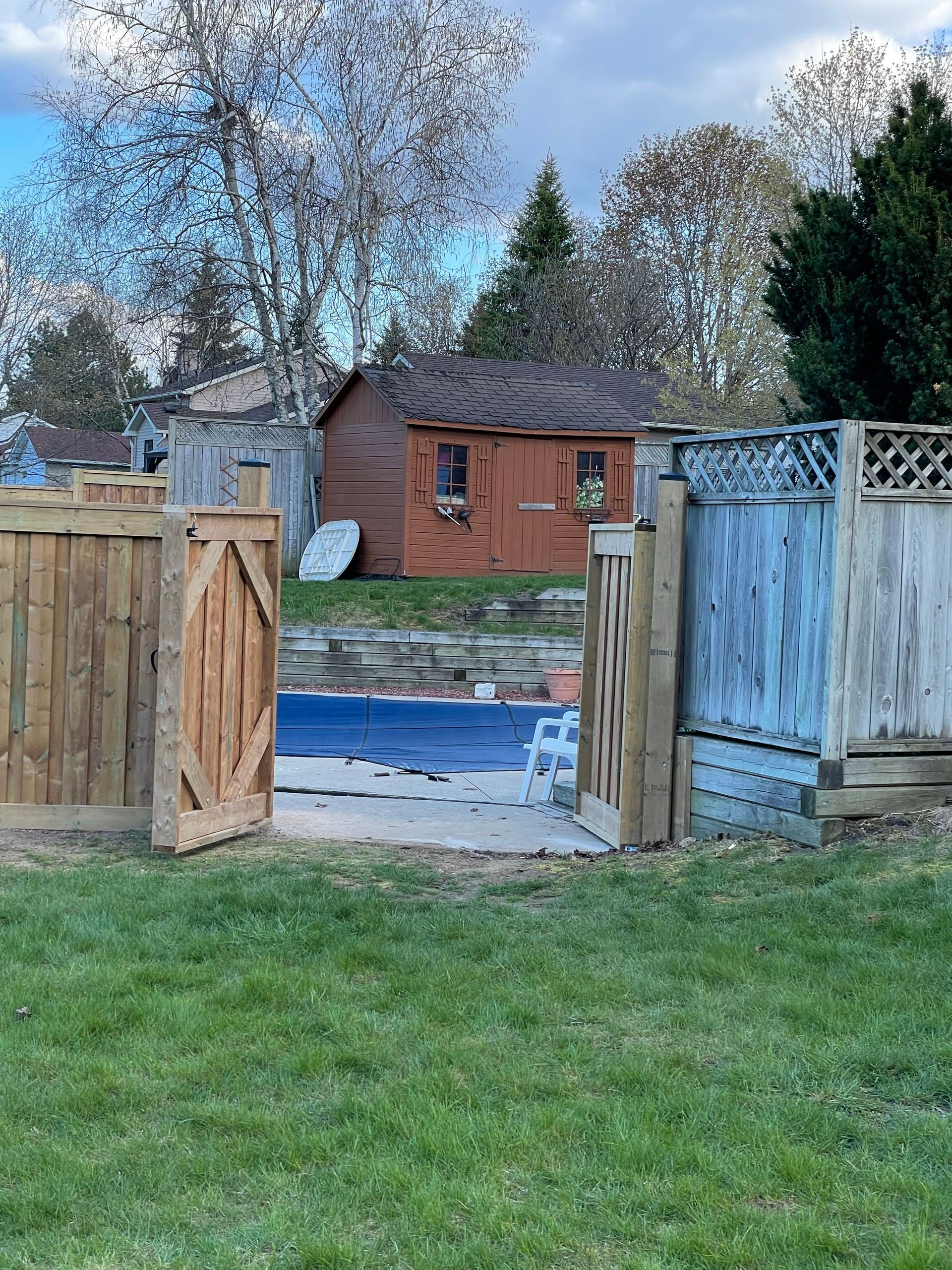 A wooden fence surrounds a swimming pool in a backyard.