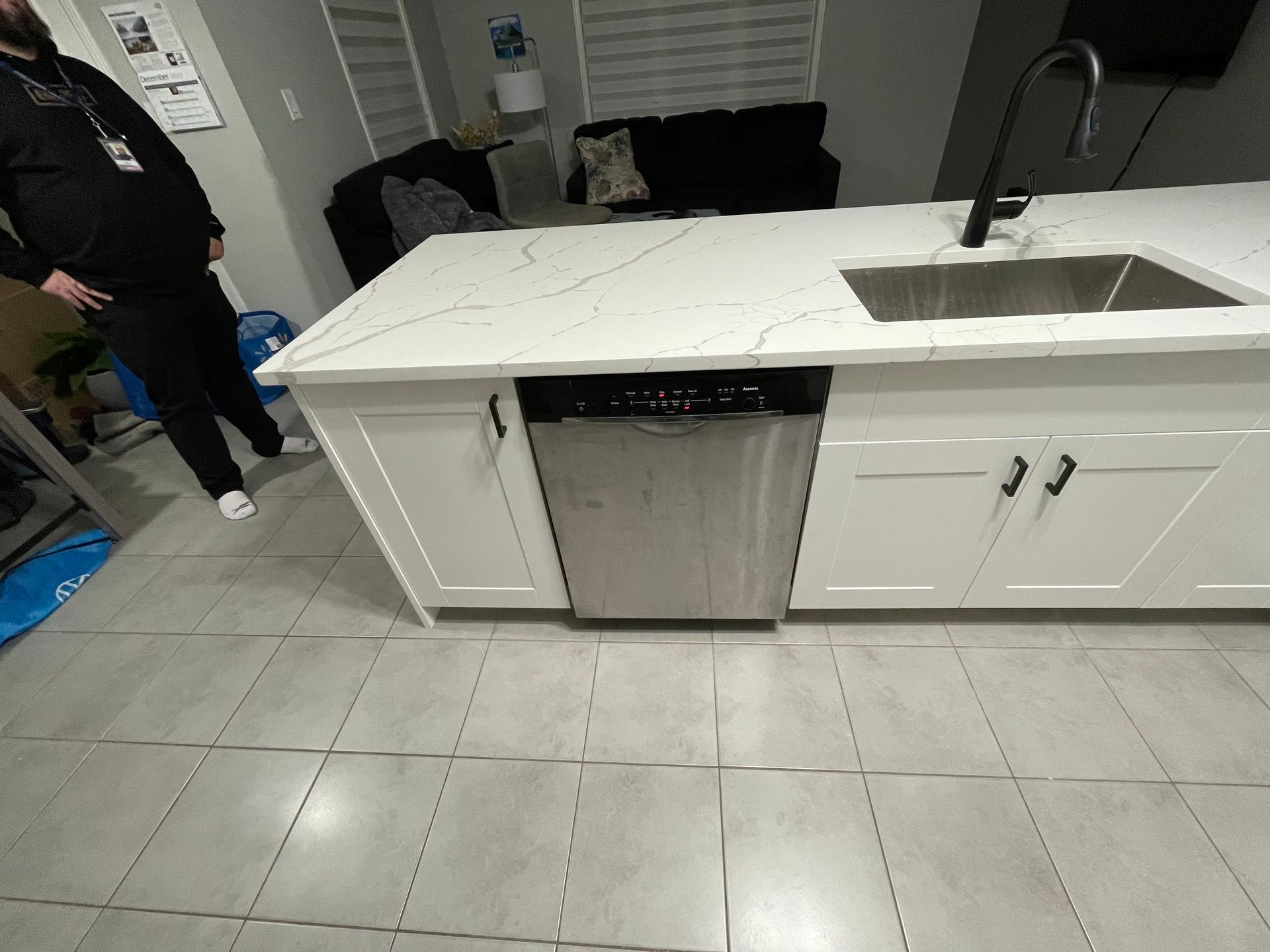 A man is standing in a kitchen with a sink and a dishwasher.