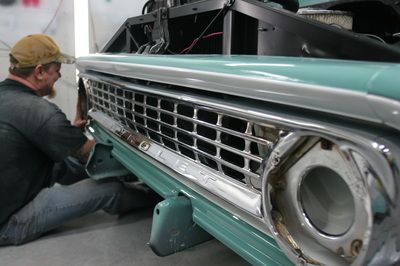 A man is working on the front of a green truck.