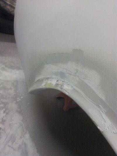 A close up of a white car fender being repaired