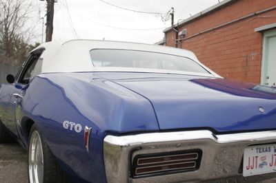 A blue gto with a white top is parked in front of a brick building