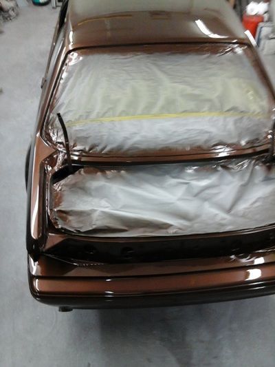 A brown car is covered in plastic wrap in a garage