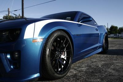 A blue car with a white stripe on the side is parked in a parking lot