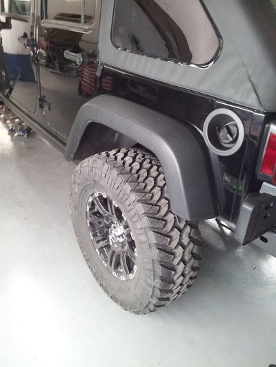 A black jeep is parked in a garage with a large tire