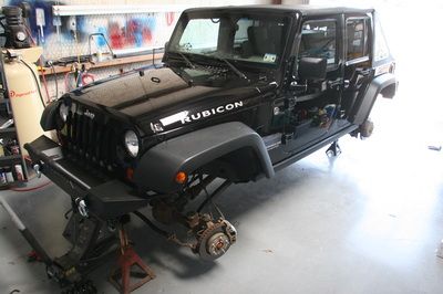A black jeep rubicon is sitting on a jack in a garage