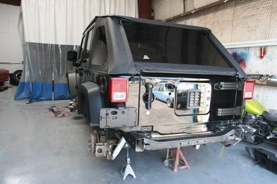 A black jeep is sitting on a jack in a garage.