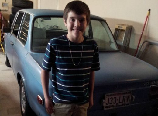 A young boy stands in front of a blue car