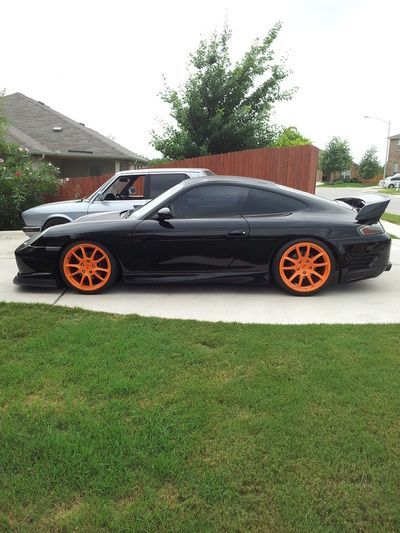 A black car with orange wheels is parked in a driveway