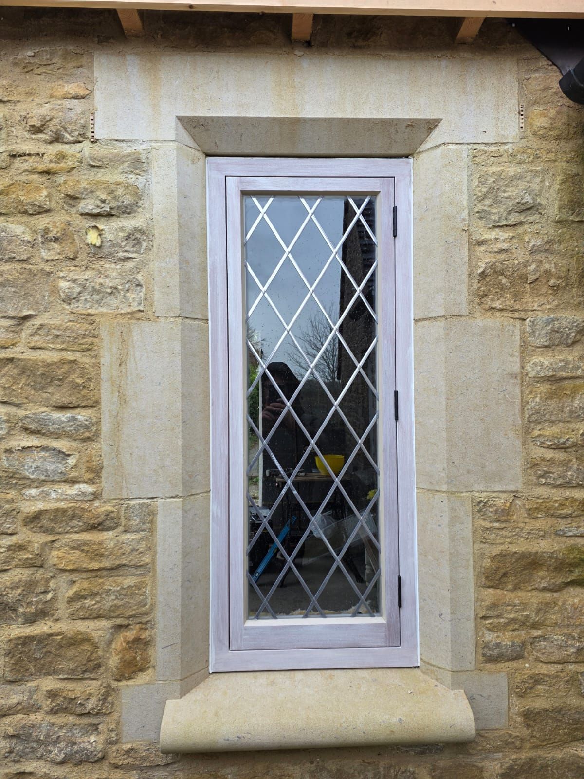 New period Narrow diamond-latticed glazed timber framed window set in a stone wall with a white frame and sill