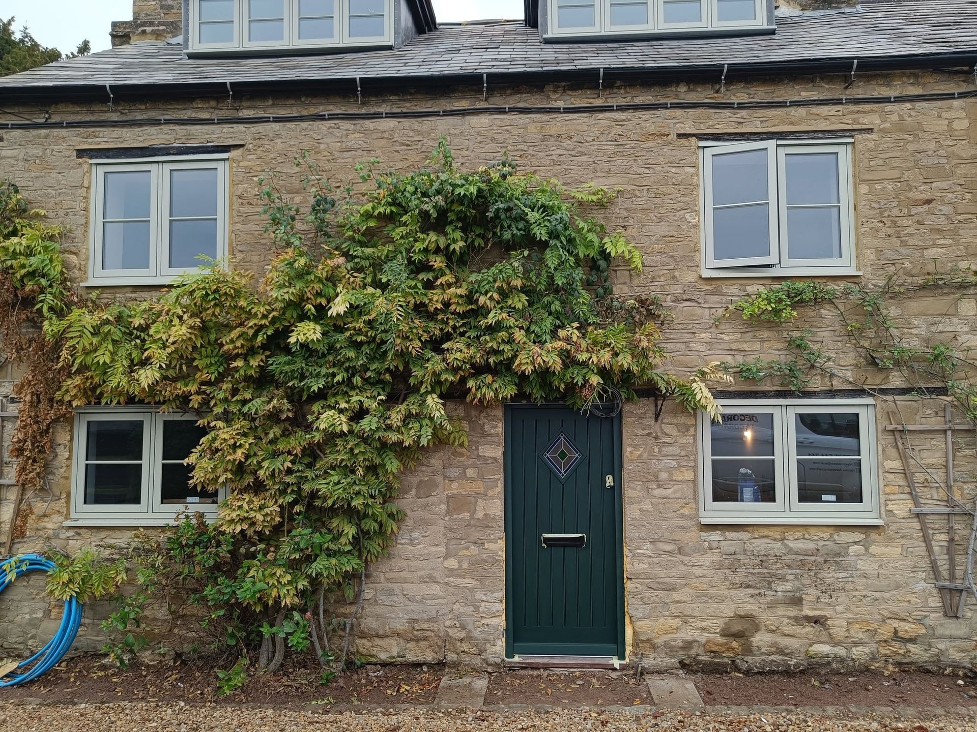 Stone cottage facade with green timber framed door, white timber windows, and ivy covering the front.