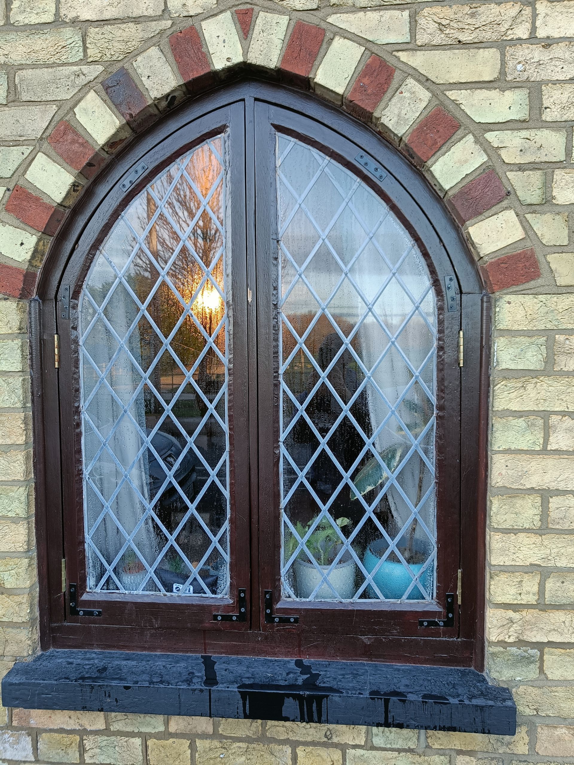 Arched brown leaded-glass window set in a brick wall with a lit lamp inside