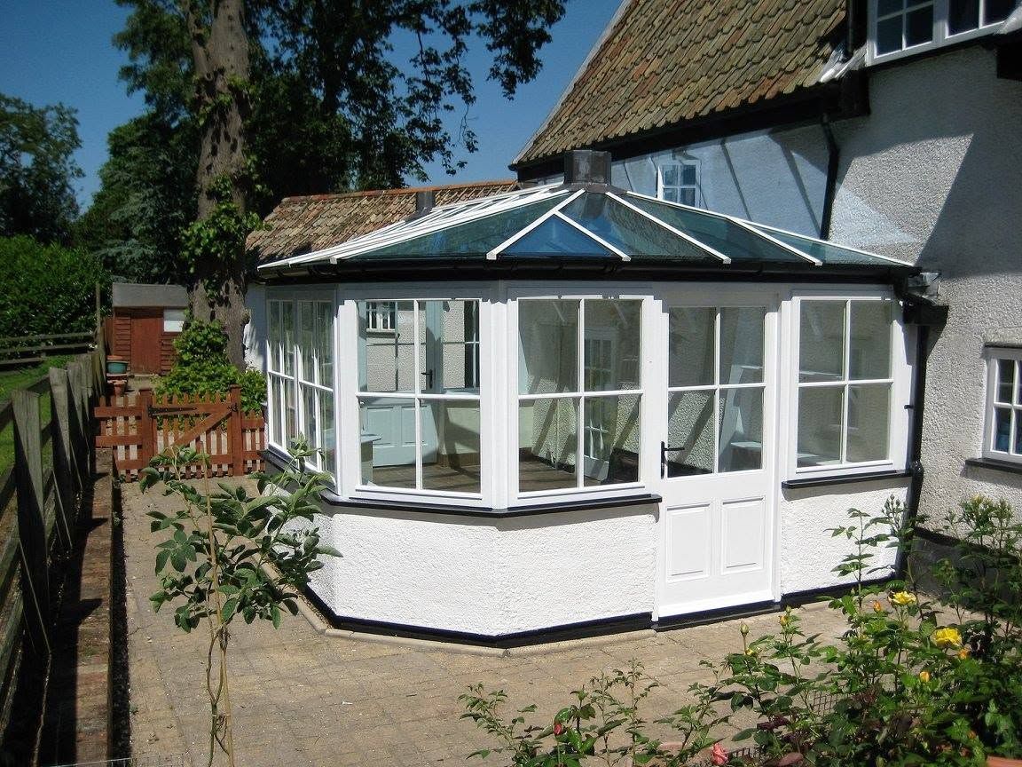 White sunroom extension with glass windows attached to a house in a garden