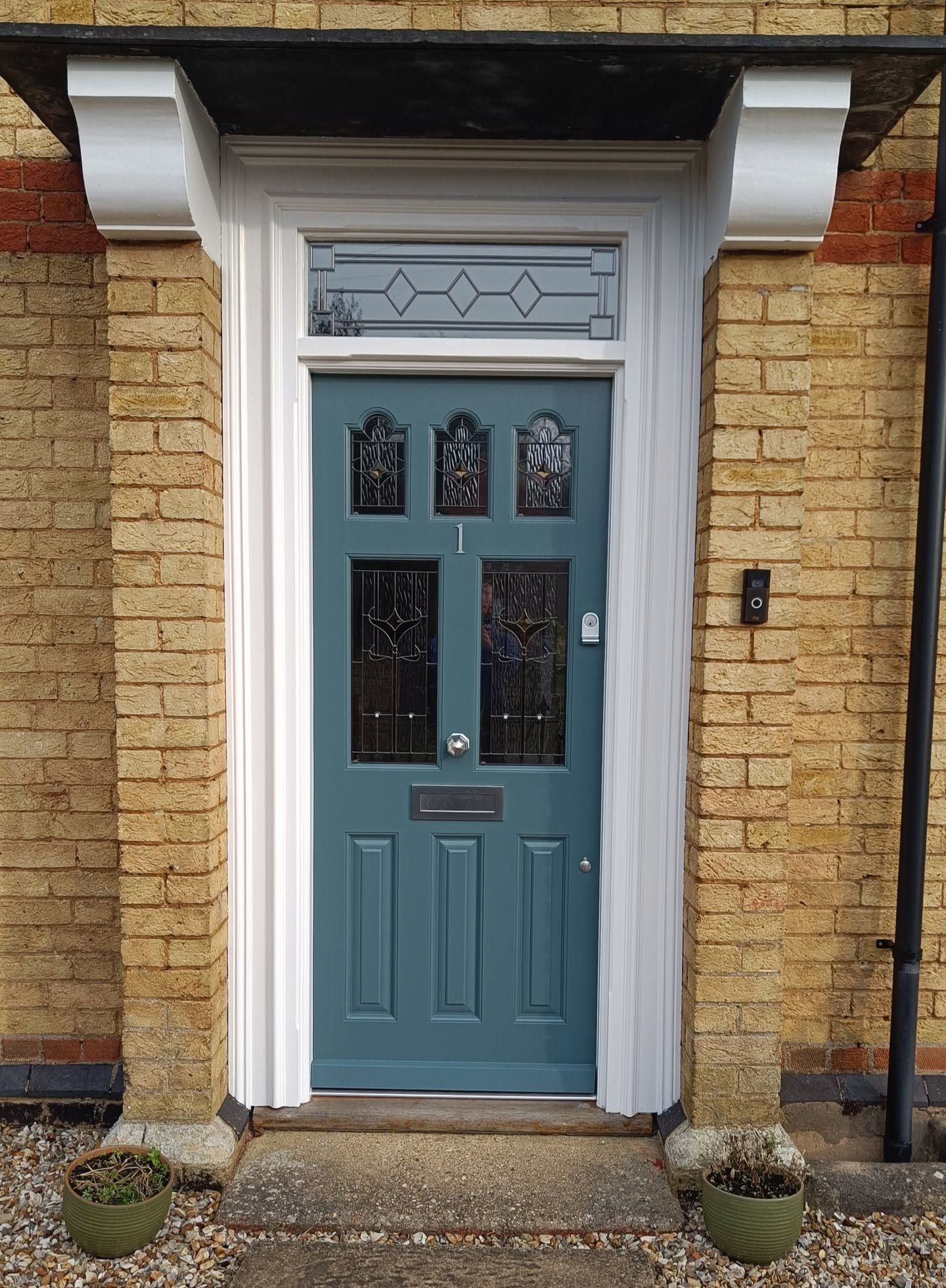Blue front timber door with decorative glass panels set in a brick house entrance