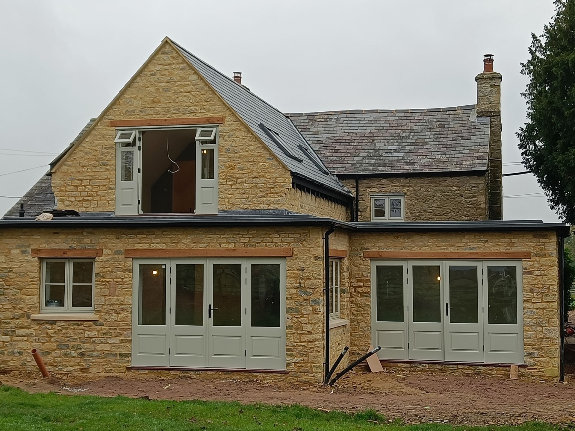 Stone house with gray roof and wooden cream-framed windows under an overcast sky