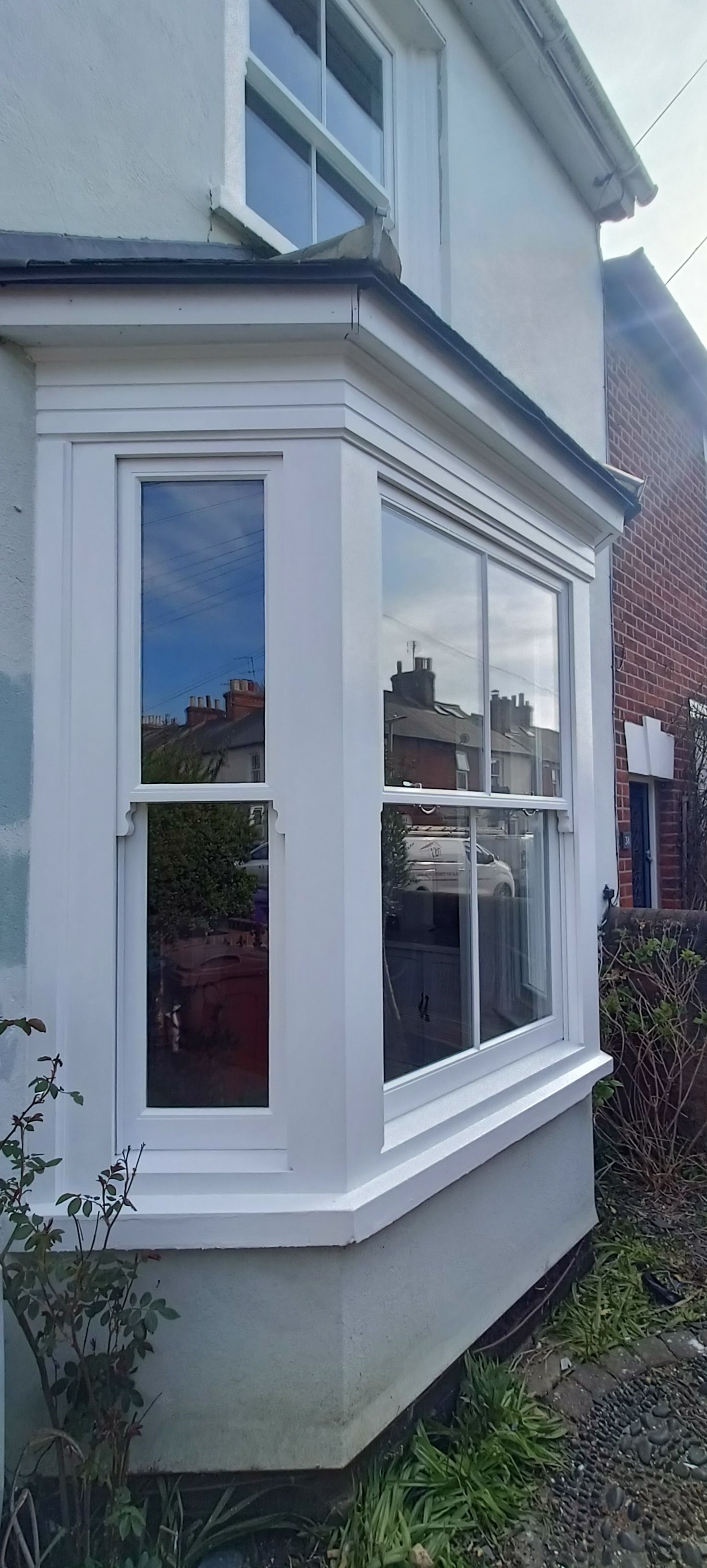 White bay window on a gray house exterior with reflections in the glass