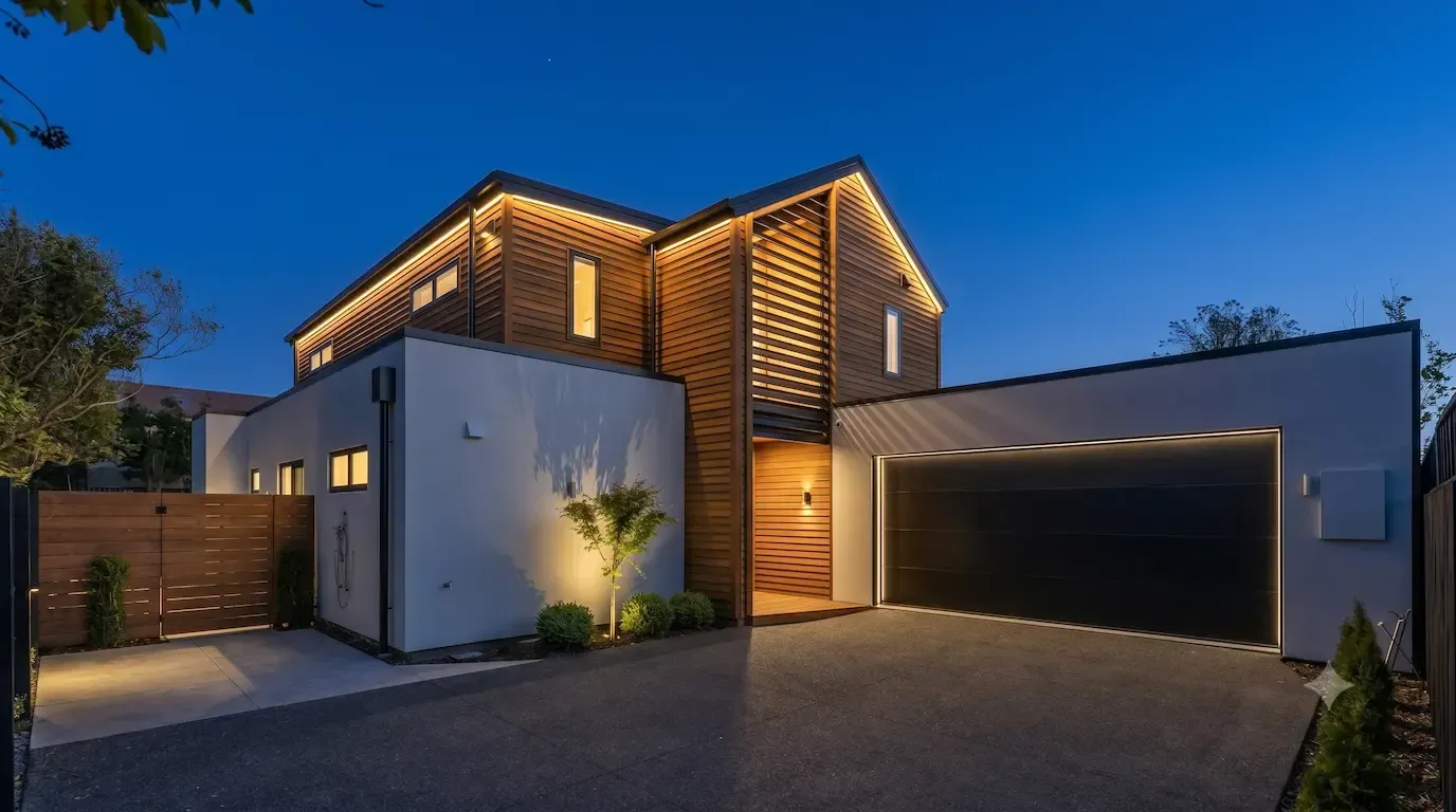 Modern two-story house at dusk with warm exterior lighting and a large garage door