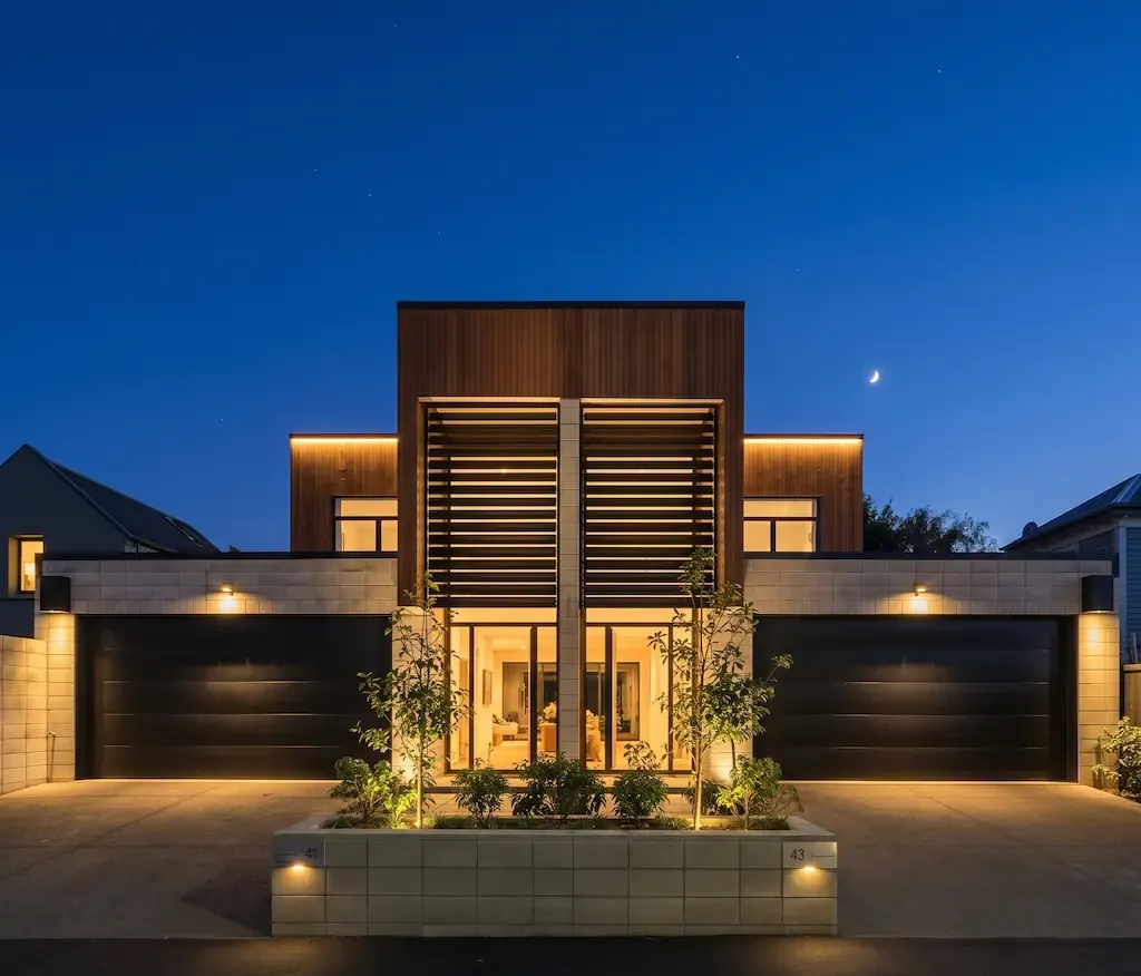 Modern luxury house at dusk with warm exterior lighting and symmetrical landscaping