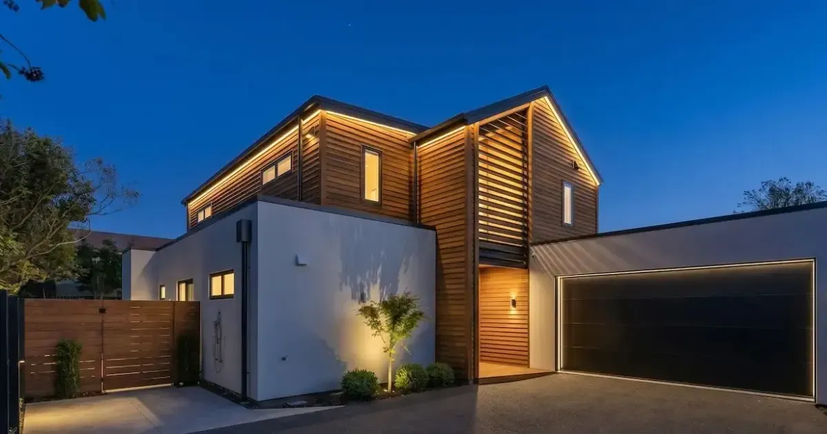 Modern two-story house with white walls, wood siding, and a brick patio in a sunny yard
