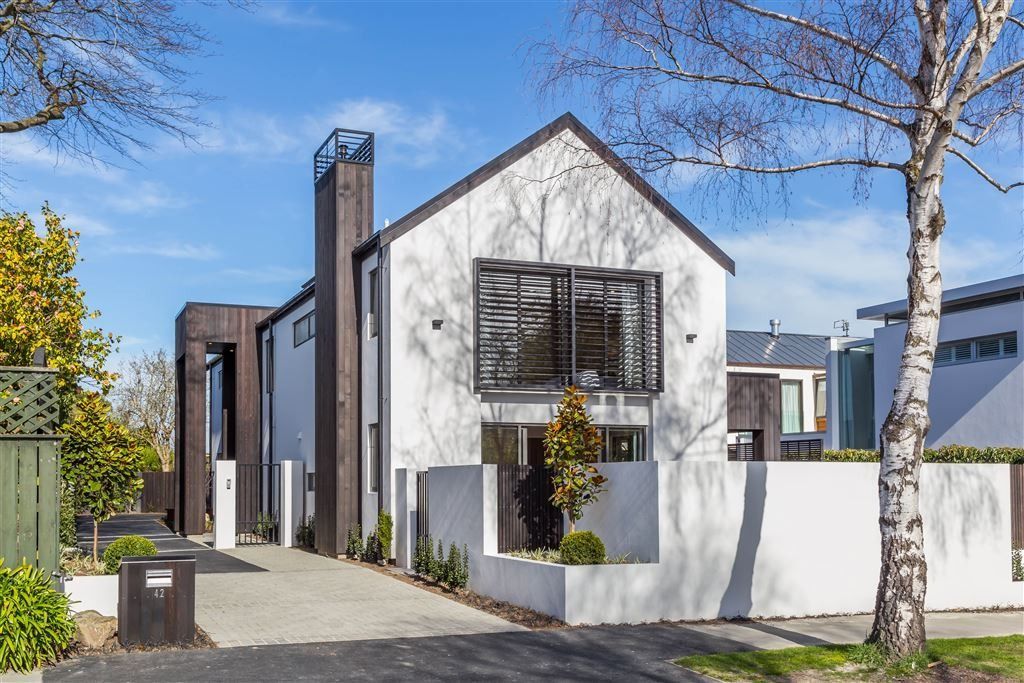 Modern white house with dark wood accents, front yard, and trees on a sunny street