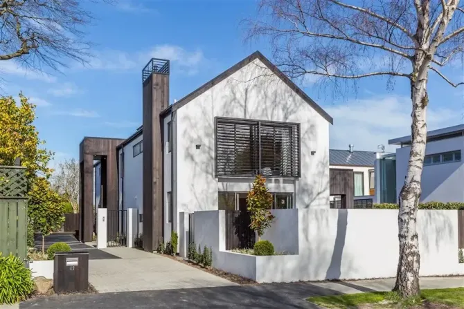 Modern white house with dark trim, driveway, and leafless trees behind a low white wall.