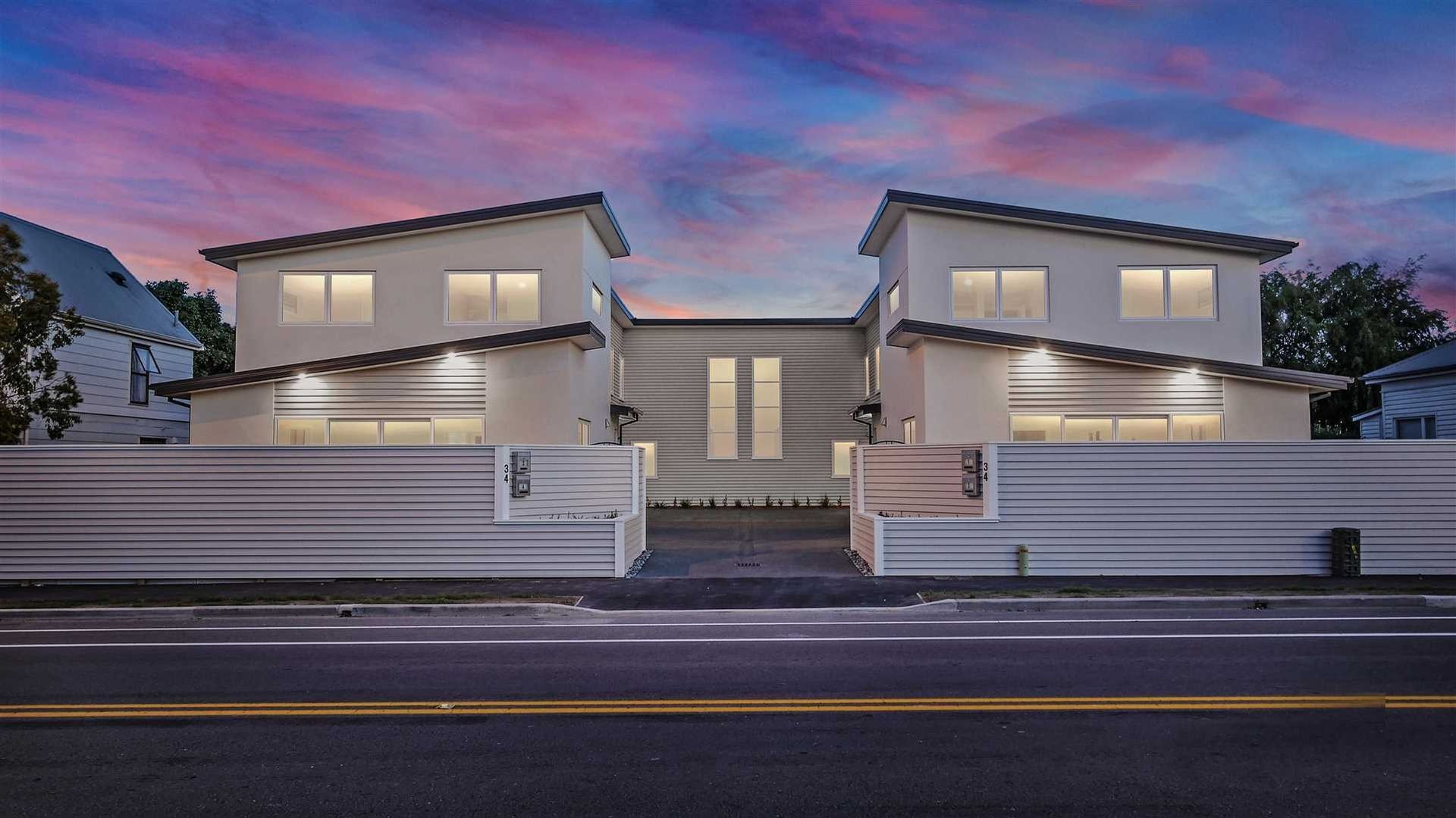 Modern two-story house with white fencing at dusk, lit windows, and a pink-blue sky