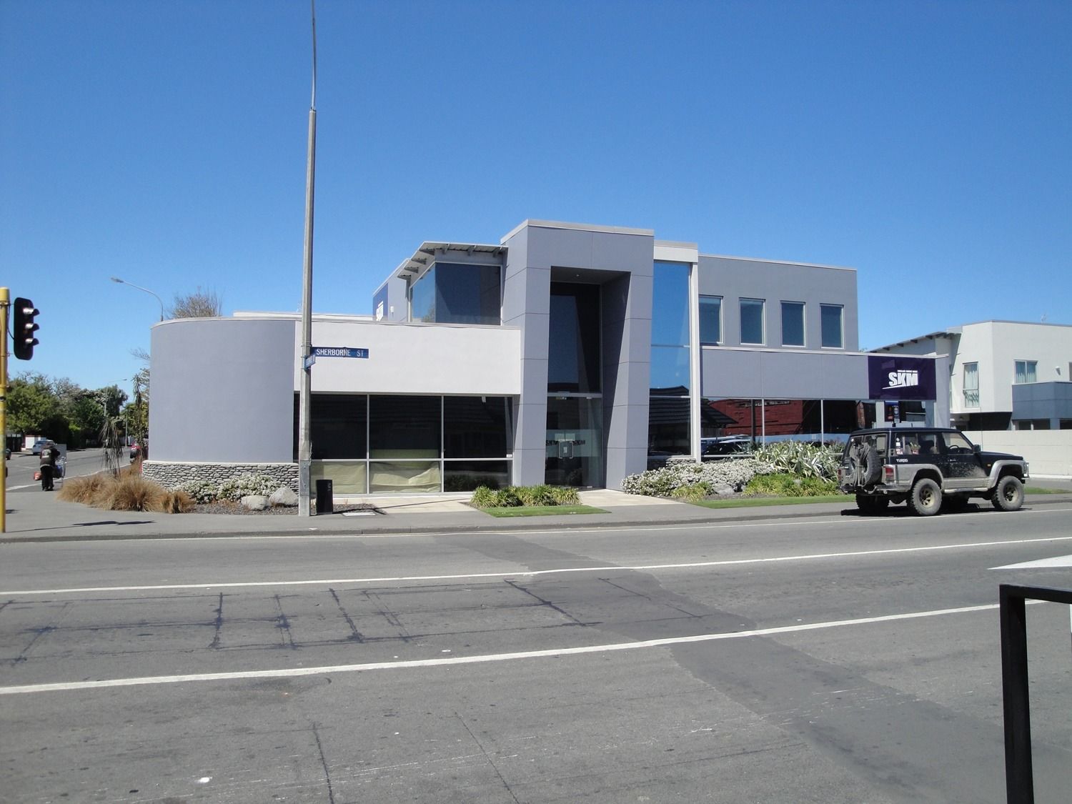 Modern gray commercial building on a sunny street with a parked Jeep in front