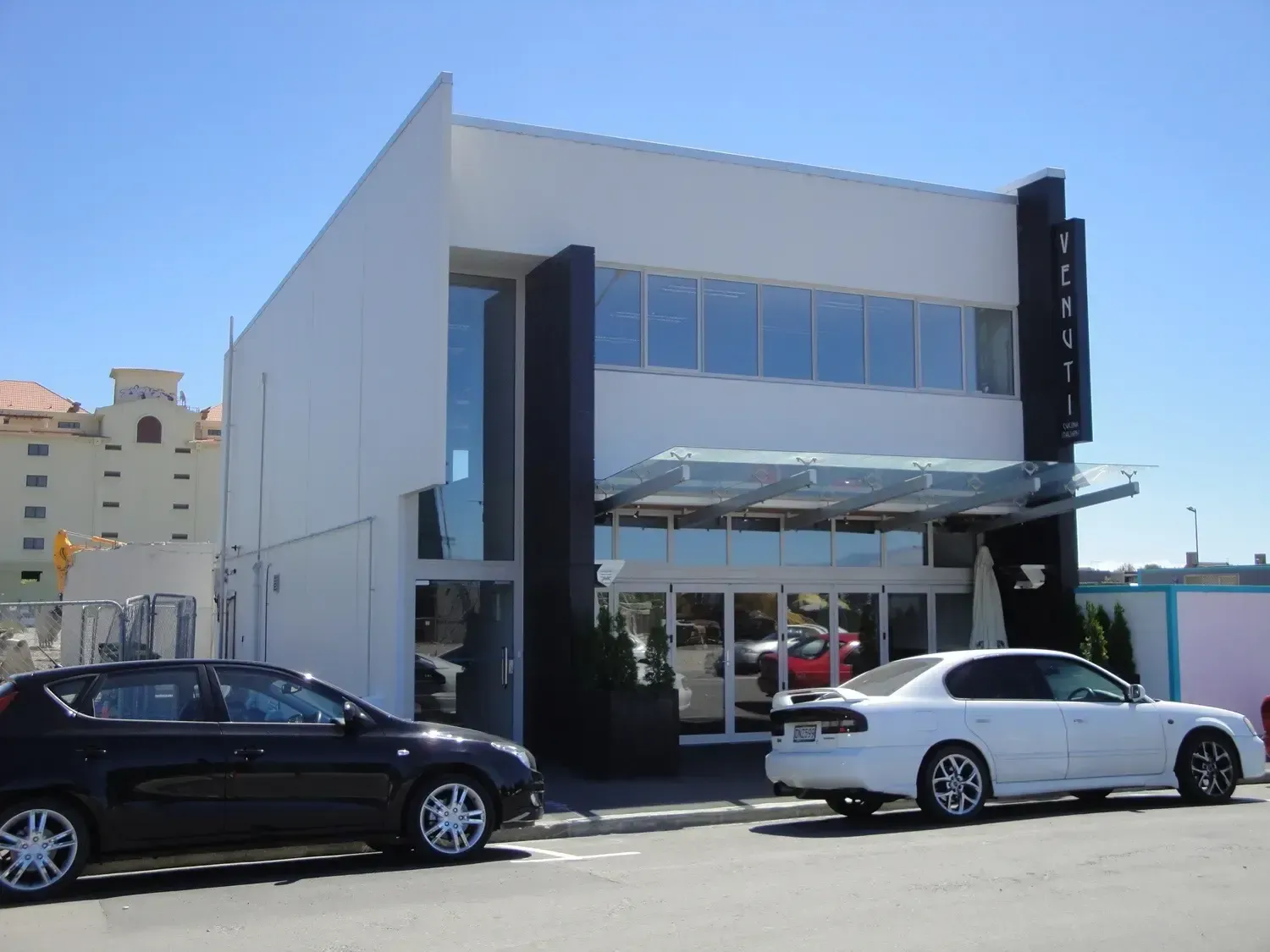 Modern glass-front commercial building with parked black and white cars outside