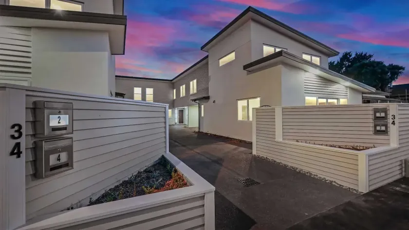 Modern townhouse entryway at dusk, with white walls, gray gate, and unit number 34 under a pink-blue sky.