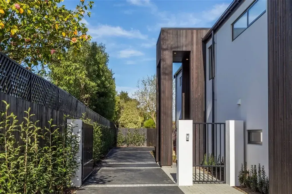 Modern house entrance with a narrow driveway, black fence, and white exterior walls under a blue sky