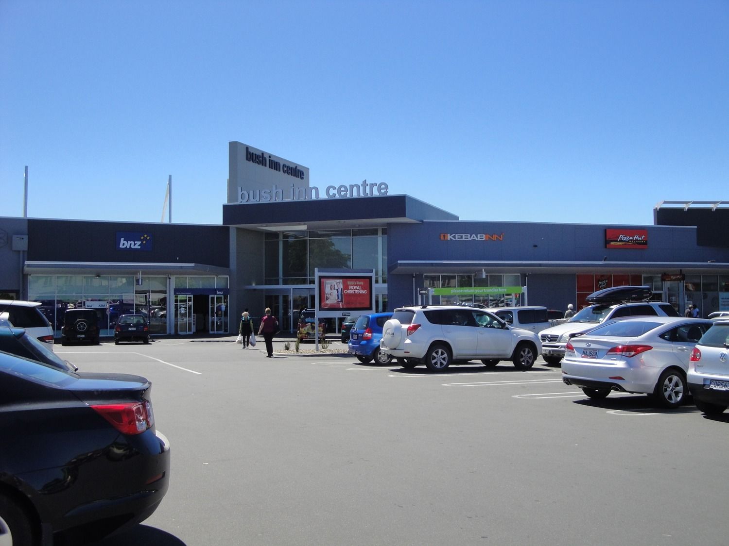 Busy shopping center parking lot with cars under a clear blue sky