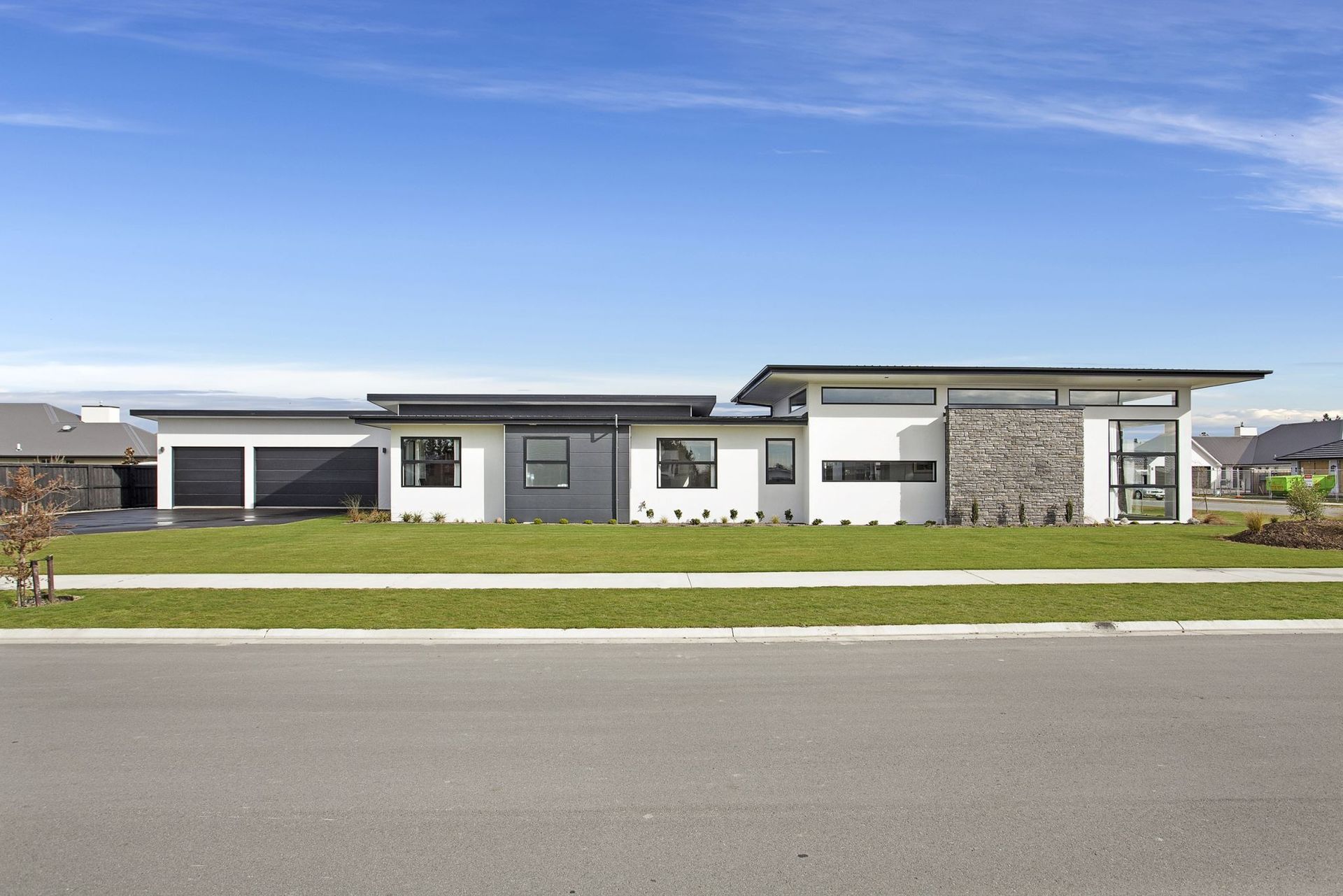 Modern single-story house with white walls, stone accents, and a flat roof under a clear blue sky