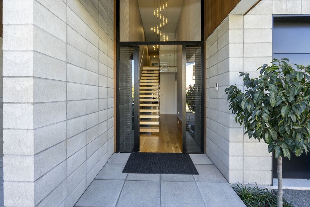 Modern building entrance with glass doors, stone walls, and a potted tree beside a walkway