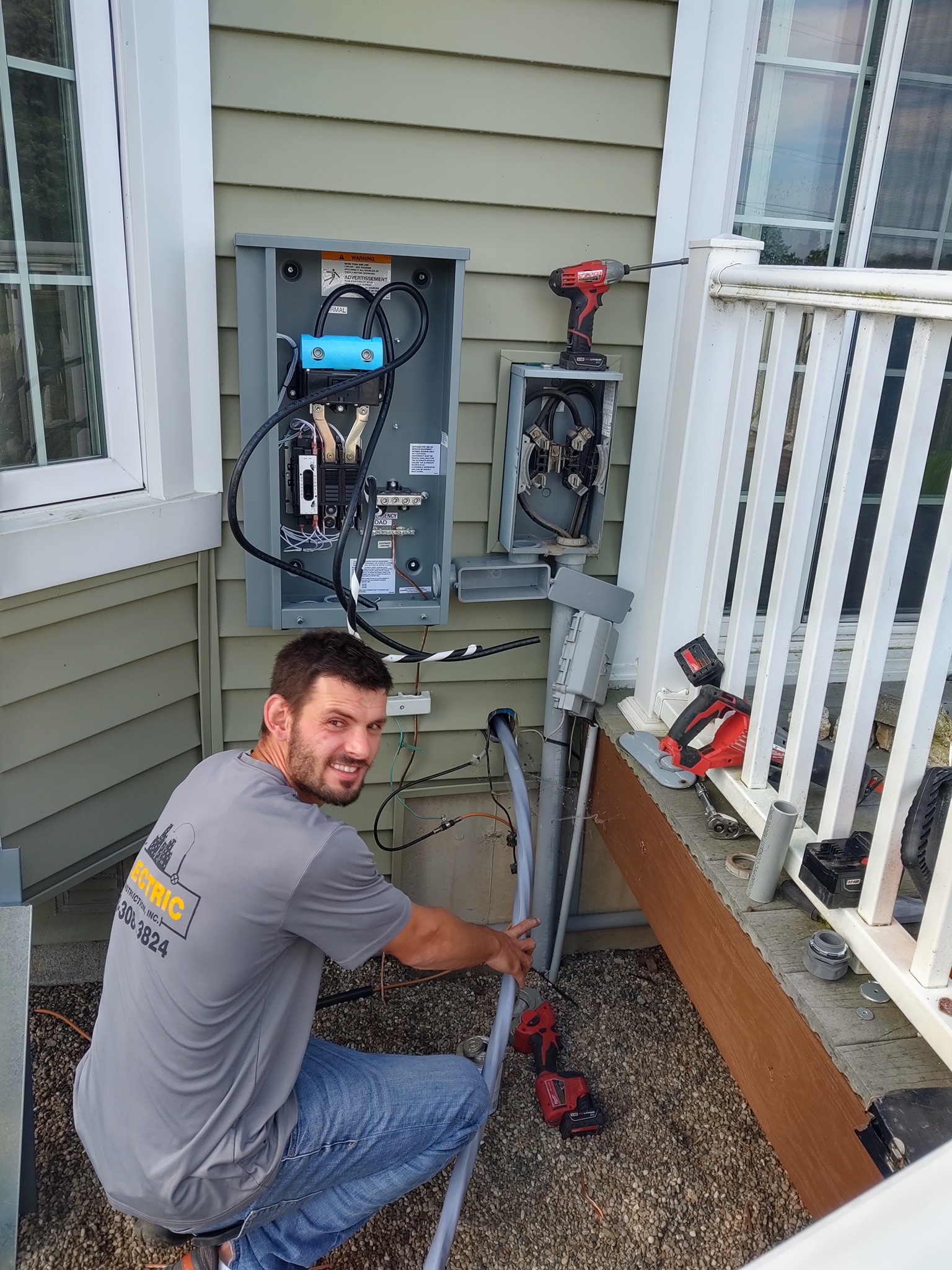 Technician kneeling by home electrical panel, working on exposed wiring outside a house.