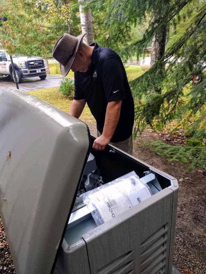 Person in a black shirt and hat empties a large outdoor trash bin on a tree-lined street.