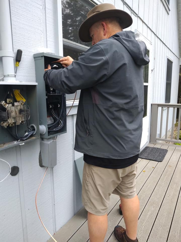 Technician working on an outdoor electrical meter and panel beside a house