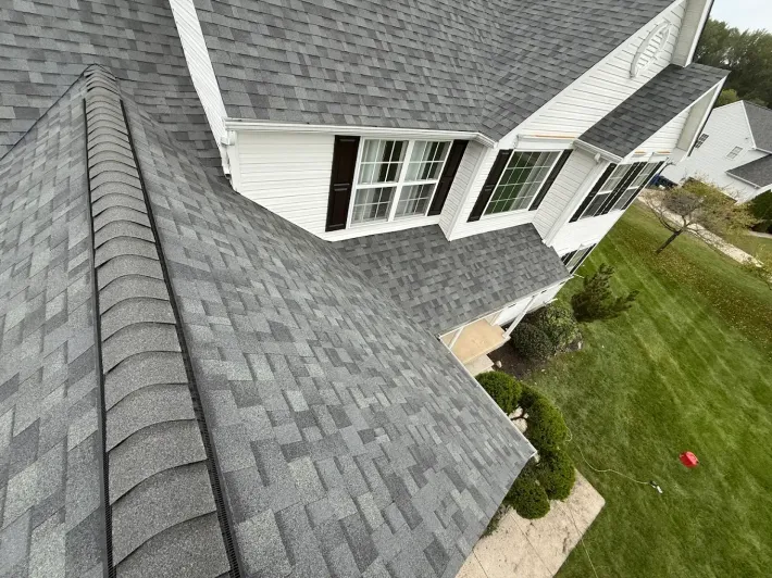 Aerial view of a house roof with gray shingles and white siding beside a green lawn