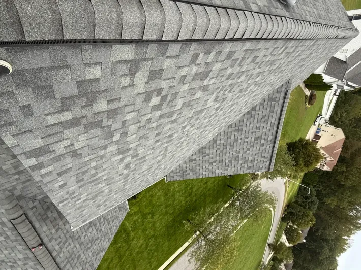 Tilted view of a gray shingled roof beside a green lawn and trees