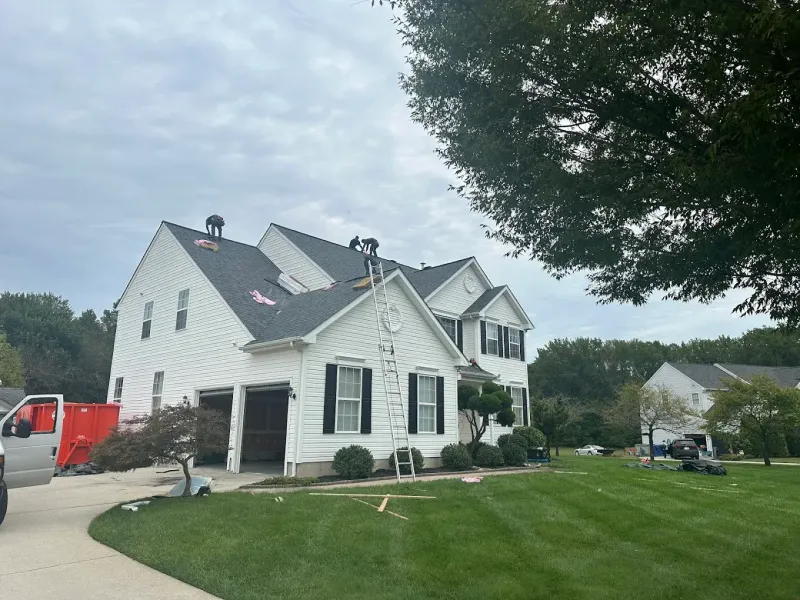 White house with black shutters and a manicured lawn on a cloudy day, with a red truck nearby.