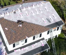 Aerial view of a house with a roof under repair, showing new shingles and a worker near a ladder.