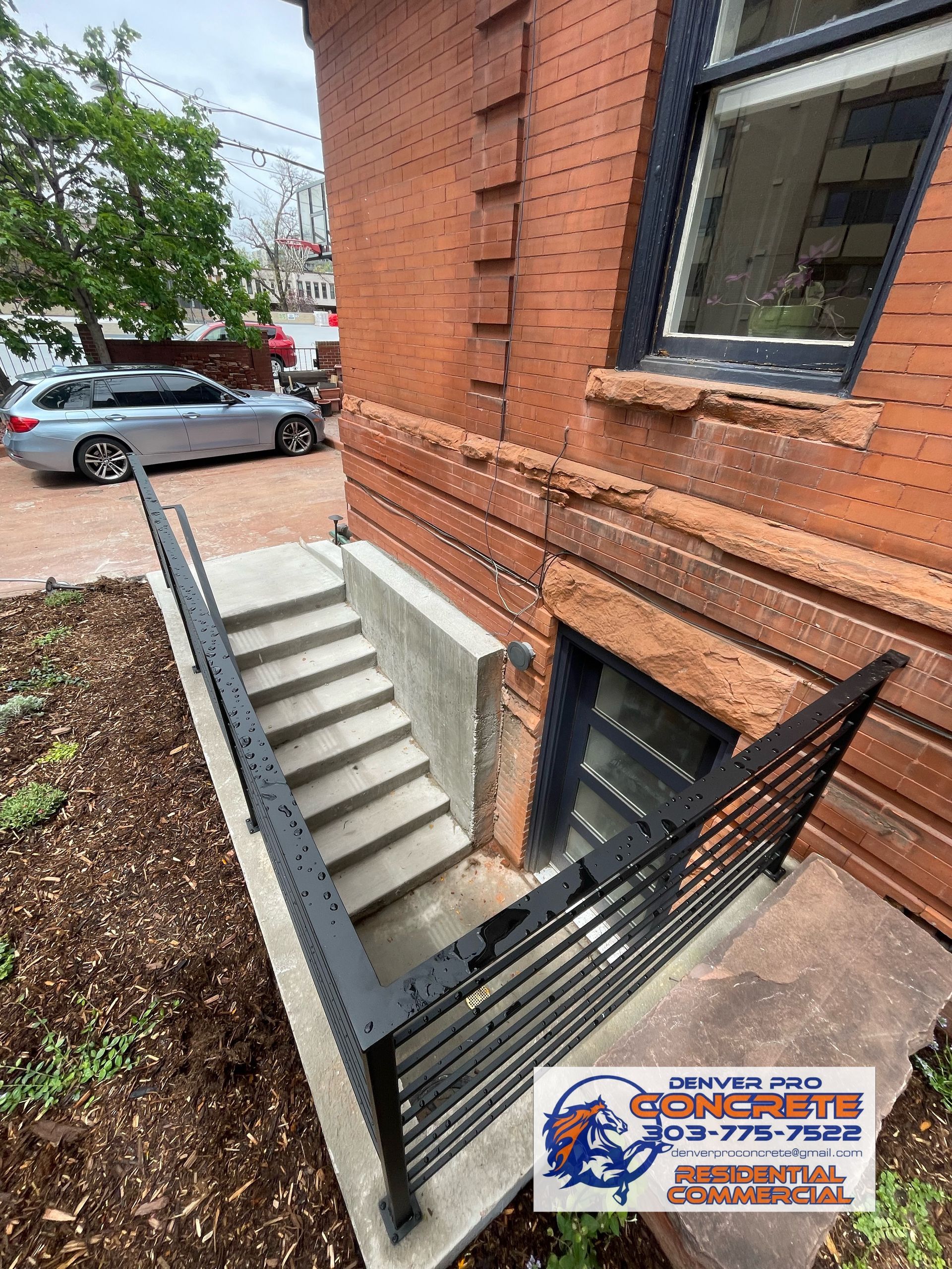A brick building with stairs leading up to a basement and a car parked in front of it.