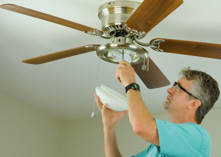 A Man In A Blue Shirt Is Fixing A Ceiling Fan — Steve Mason Electrical In Port Macquarie, NSW