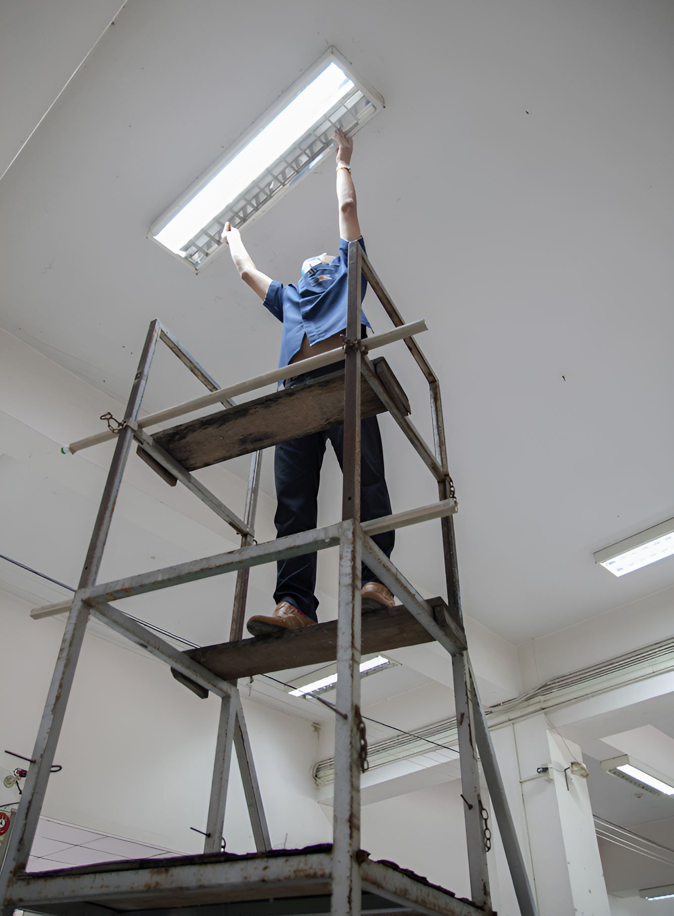 A Man Is Standing On A Scaffolding Holding A Light — Steve Mason Electrical In Port Macquarie, NSW