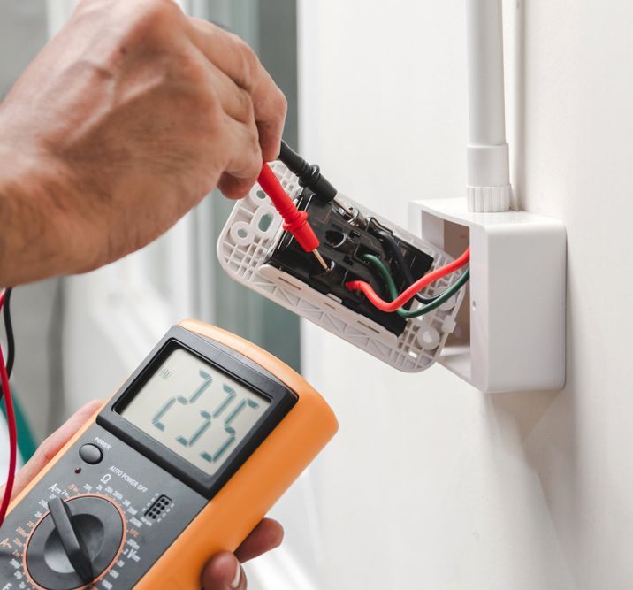 A Man Is Using A Digital Multimeter To Test An Electrical Outlet — Steve Mason Electrical In Port Macquarie, NSW