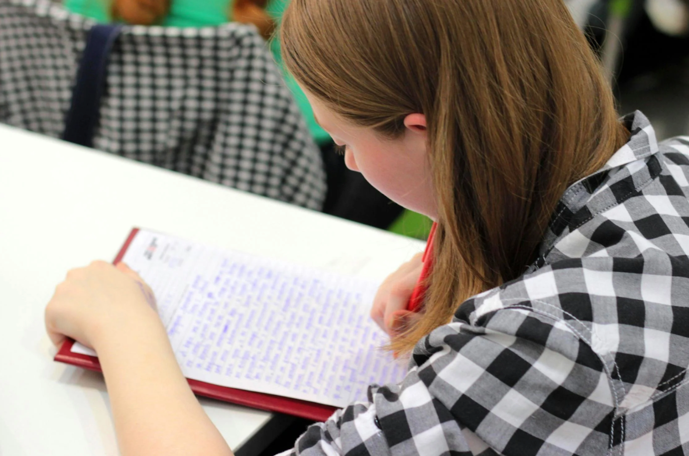 A girl is sitting at a desk writing in a notebook.