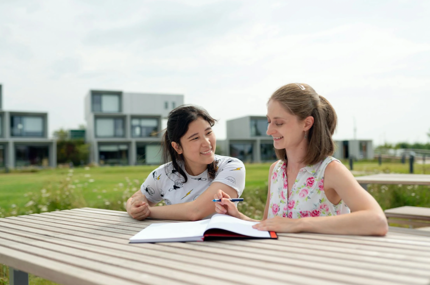 Two girls are sitting at a picnic table talking to each other.