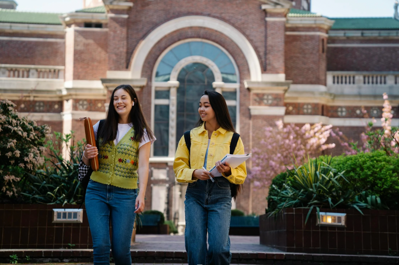 Two women are walking down a sidewalk in front of a building.